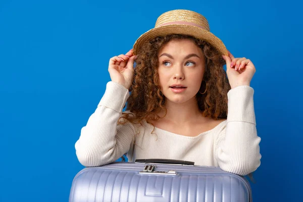 Jovem bela mulher de chapéu em férias com mala contra fundo azul — Fotografia de Stock