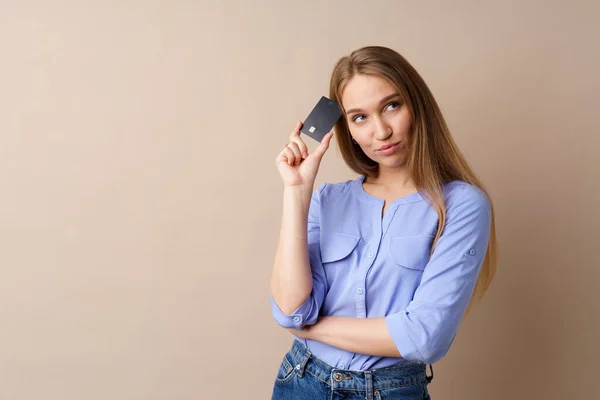 Mulher bonita segurando cartão de crédito preto contra fundo bege — Fotografia de Stock