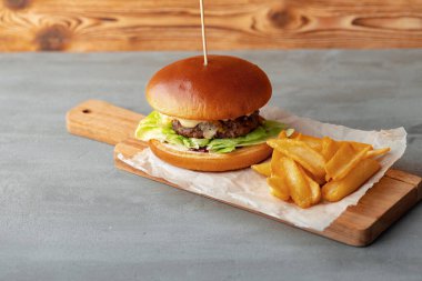 Gri ahşap arka planda taze hamburger ve patates dilimleri.