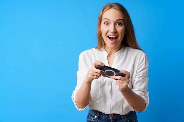 Jovem mulher positiva jogando jogos no smartphone contra fundo azul — Fotografia de Stock