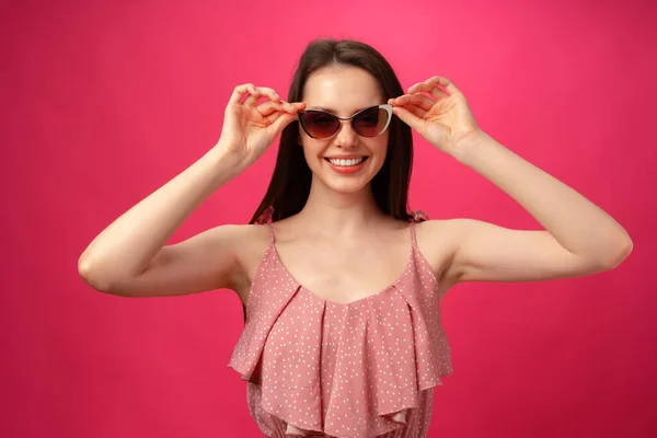 Jeune femme brune décontractée en lunettes de soleil sur fond rose — Photo