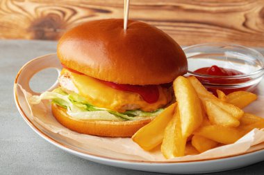 Gri ahşap arka planda taze hamburger ve patates dilimleri.