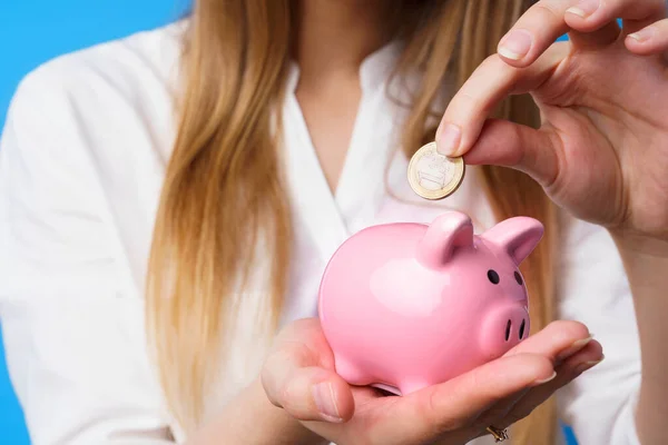 Frau steckt Geld in rosa Sparschwein vor blauem Hintergrund — Stockfoto