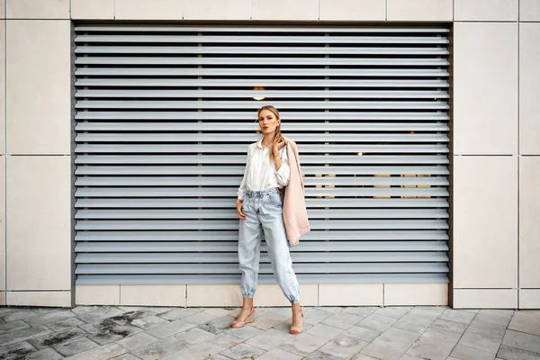 Stijlvol meisje in jeans en witte katoenen blouse poseren in de buurt van grijze muur — Stockfoto