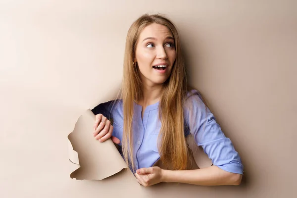 Hermosa mujer joven mirando a través de un agujero en papel beige — Foto de Stock