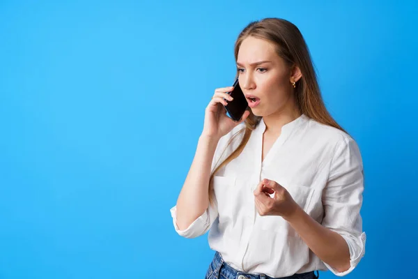 Mulher infeliz falando ao telefone estressado com más notícias, fundo azul — Fotografia de Stock