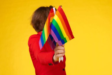 Parlak arkaplanda küçük LGBT bayrağı tutan tanınmayan genç bir kadın.