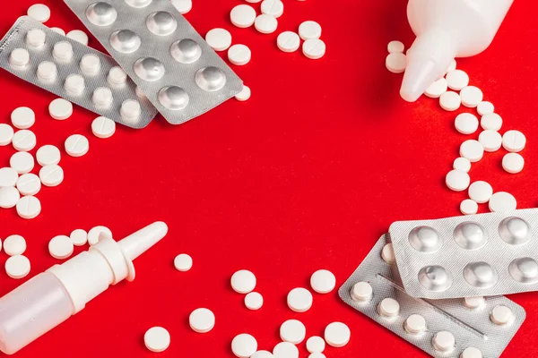 Білі таблетки, що виливаються з верхньої білої пляшки на червоному тлі — стокове фото