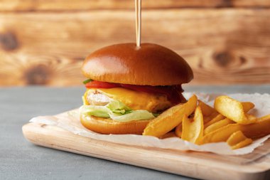 Gri ahşap arka planda taze hamburger ve patates dilimleri.