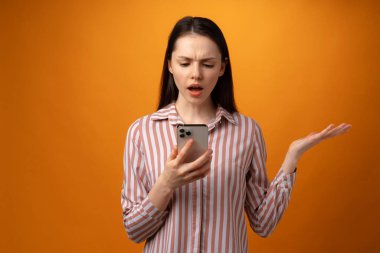 Stresli, hayal kırıklığına uğramış, elinde akıllı telefon tutan genç bir kadın. Kötü haber almış, sarı arka plan.