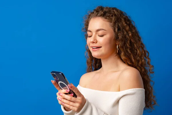 Jovem mulher encaracolada usando seu smartphone contra fundo azul — Fotografia de Stock