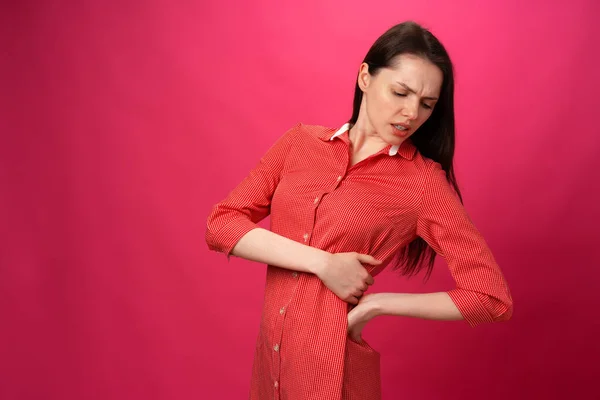 Morena menina tem dor nas costas contra fundo rosa — Fotografia de Stock