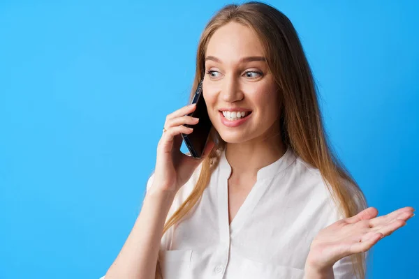 Glücklich lächelnde junge Frau telefoniert vor blauem Hintergrund — Stockfoto