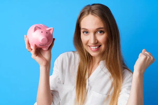 Krásná usmívající se mladá žena s prasátko banka na modrém pozadí — Stock fotografie