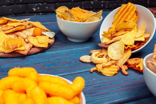 Tipos diferentes de comida chatarra, palos salados, galletas saladas en la mesa de madera en bodegón — Foto de Stock