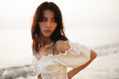 Gün batımında kumsalda genç esmer bir kadının portresi.