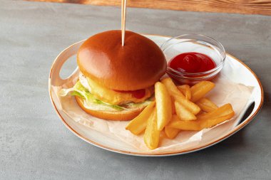 Gri ahşap arka planda taze hamburger ve patates dilimleri.