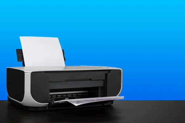 Impressora laser compacta em mesa preta contra fundo azul — Fotografia de Stock