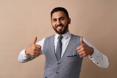 Mutlu genç Arap adam bej arka planda başparmak işareti gösteriyor