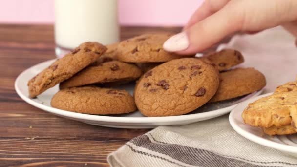 Female hand taking chocolate chip cookie from a plate on wooden table, close up — Stock Video