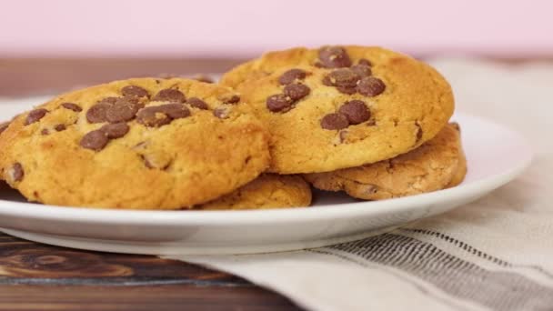 Montón de galletas de chispas de chocolate en plato blanco en mesa de madera — Vídeo de stock