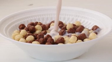 Kahvaltıda çikolatalı mısır gevreği olan bir kaseye süt dökülüyor.