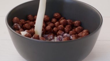 Kahvaltıda çikolatalı mısır gevreği olan bir kaseye süt dökülüyor.
