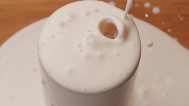 Yoghurt pouring into a glass and brim over the edgeon table, close up — Stock Video