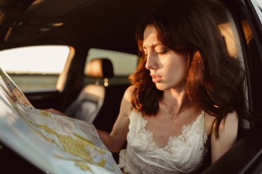 Kırsalda arabasında oturmuş haritaya bakan kayıp genç bir kadın.