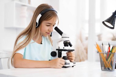 Evde online ders sırasında mikroskop kullanan genç bir kız.