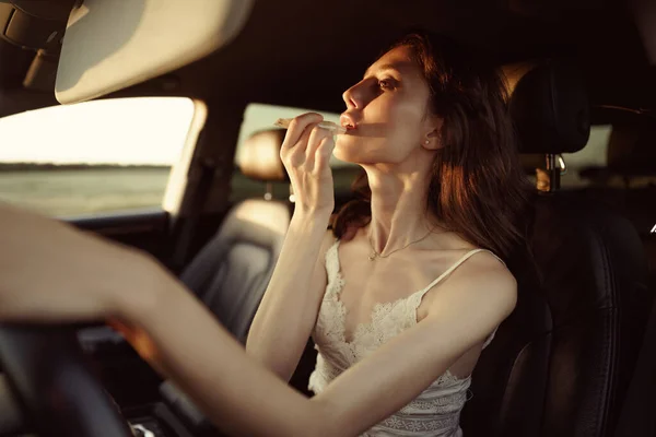 Schöne junge Kaukasierin bemalt Lippen auf dem Beifahrersitz ihres Autos — Stockfoto