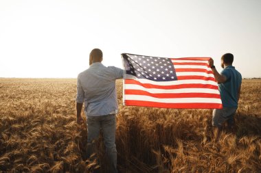 İki vatansever buğday tarlasının üzerinde Amerikan bayrağı taşıyor.