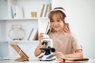 Evde online ders sırasında mikroskop kullanan genç bir kız.