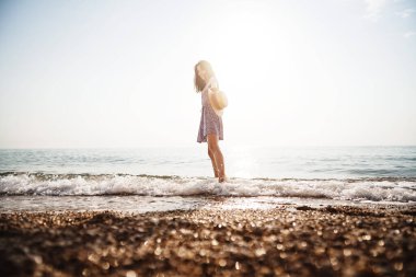 Yalnız genç kadın gün batımında sahilde yürüyor.