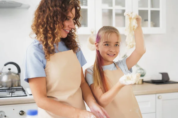 Menina adolescente ajudando sua mãe a cozinhar massa em sua cozinha em casa — Fotografia de Stock