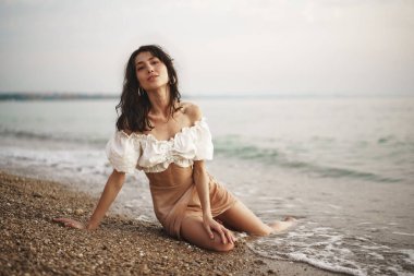 Genç ve rahat bir kadın boş kumsalda tek başına oturuyor.