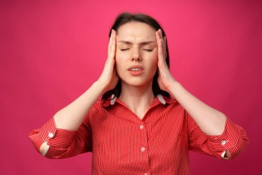 Başı pembe arka plana değen, başı ağrıyan genç kadın.