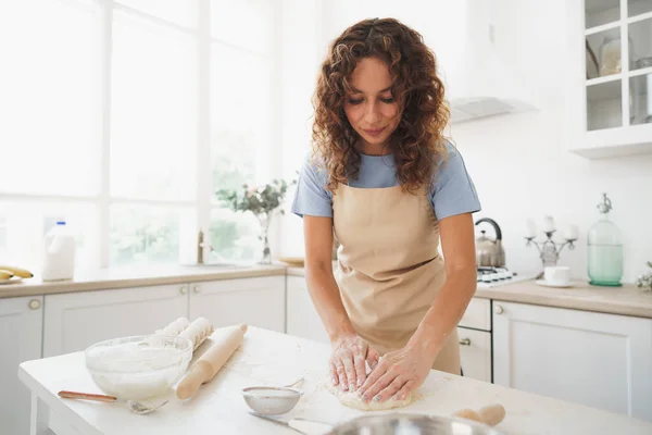 Кудрявая женщина домохозяйка готовит тесто на кухне дома — стоковое фото