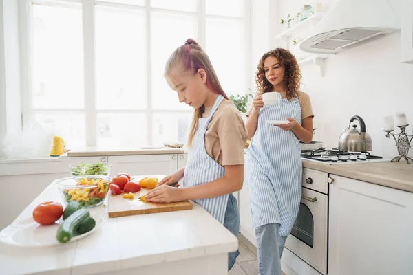 Anyu tanítja a tini lányát zöldségsalátát főzni a konyhában. — Stock Fotó