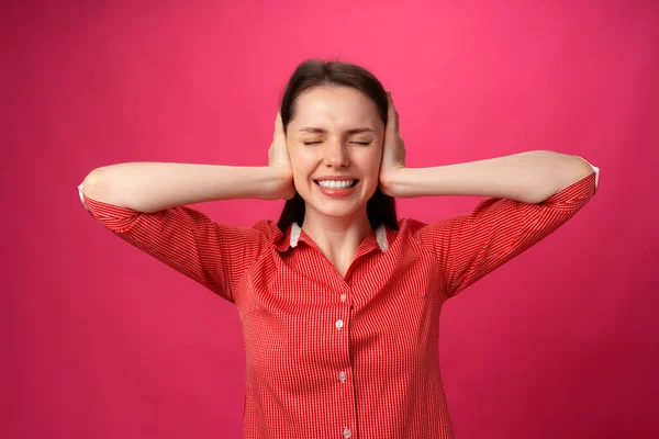 Beautiful young woman gestures she doesnt want to hear and holds hands on her ears against pink background — Stock Photo, Image
