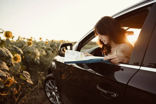 Verlorene junge Frau sitzt in ihrem Auto auf dem Land und schaut auf Landkarte — Stockfoto