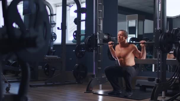 Senior fit hombre culturista haciendo sentadillas de barra en el gimnasio — Vídeo de stock