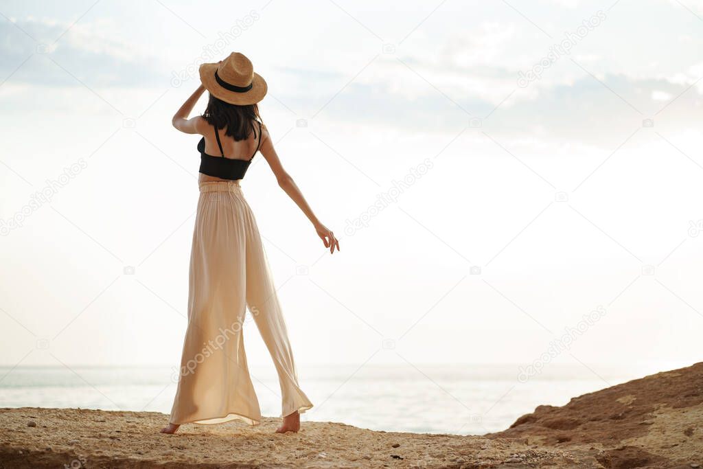 Young stylish woman standing on cliff at the sea at sunset
