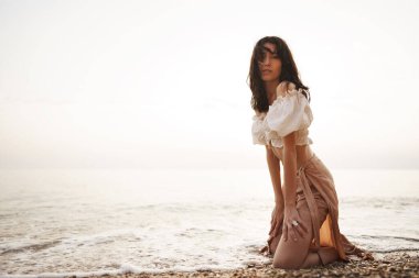 Genç ve rahat bir kadın boş kumsalda tek başına oturuyor.