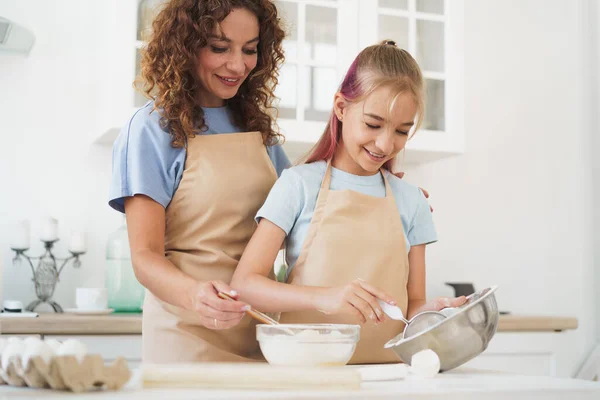 Menina adolescente ajudando sua mãe a cozinhar massa em sua cozinha em casa — Fotografia de Stock