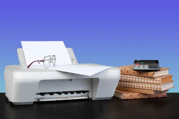 Kompaktowa drukarka laserowa na czarnym biurku na niebieskim tle — Zdjęcie stockowe