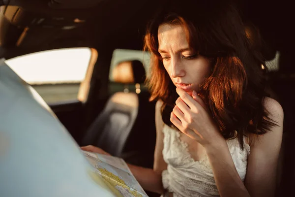 Verlorene junge Frau sitzt in ihrem Auto auf dem Land und schaut auf Landkarte — Stockfoto