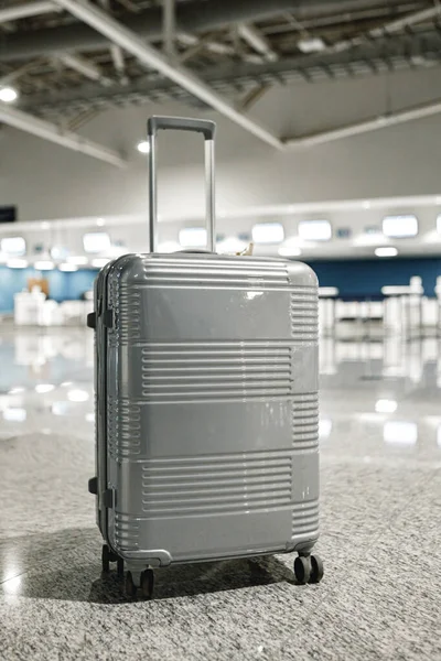 Harmaa matkalaukku tyhjässä lentokenttähallissa — kuvapankkivalokuva