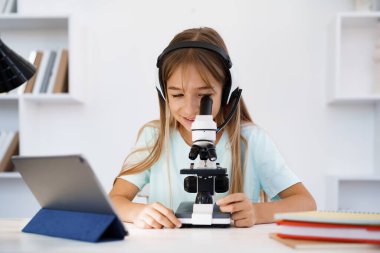 Evde online ders sırasında mikroskop kullanan genç bir kız.