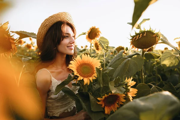 Усміхнена жінка в капелюсі стоїть на полі соняшників на заході сонця — стокове фото